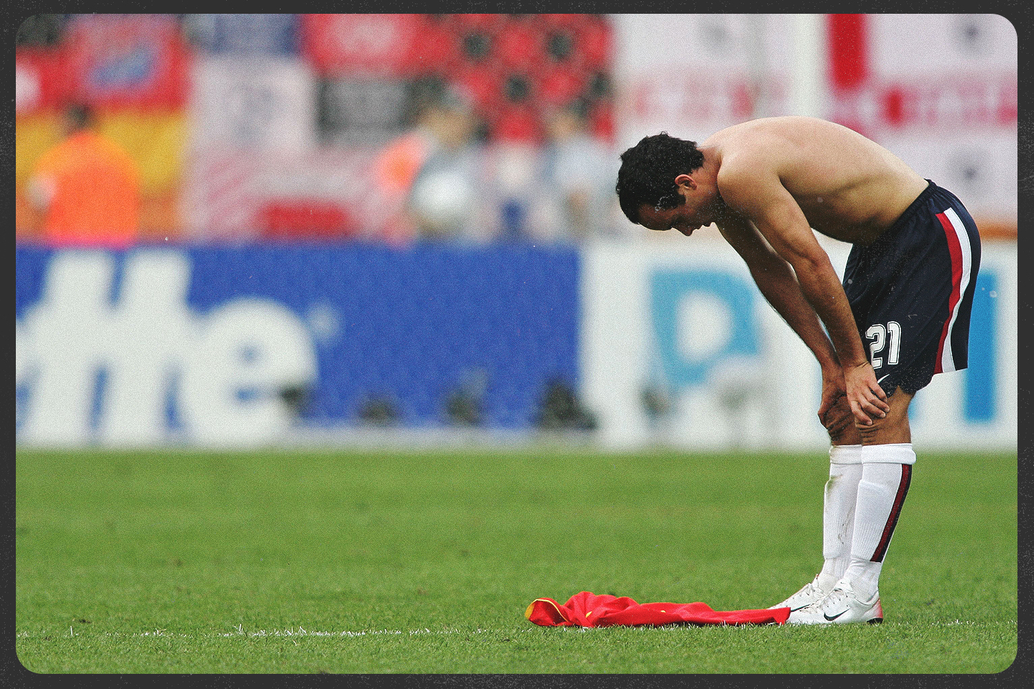Landon Donovan with his shirt off and his hands on his knees in exhaustion.