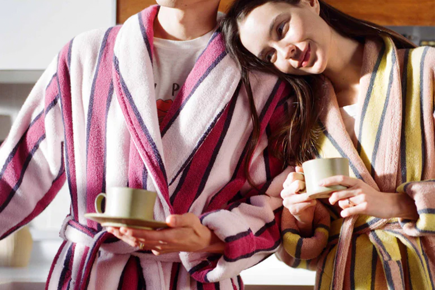A man and a woman in striped bath robes holding cups of coffee