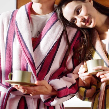 A man and a woman in striped bath robes holding cups of coffee