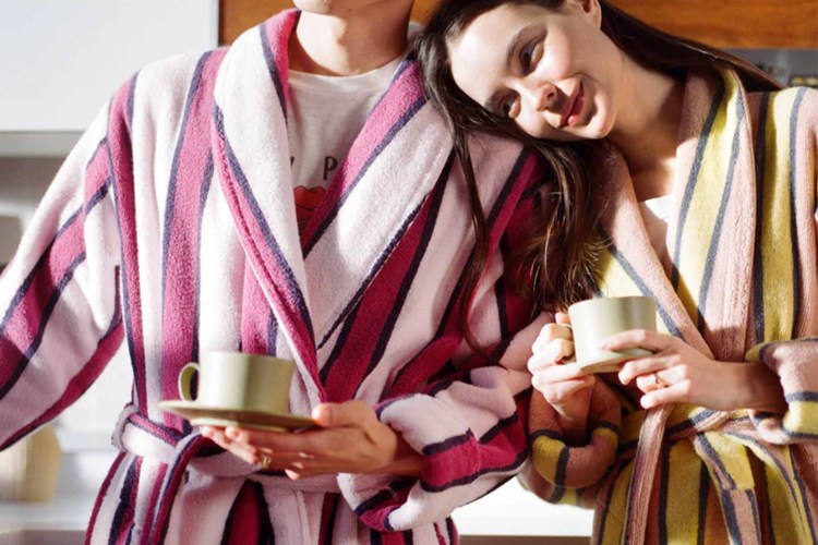 A man and a woman in striped bath robes holding cups of coffee
