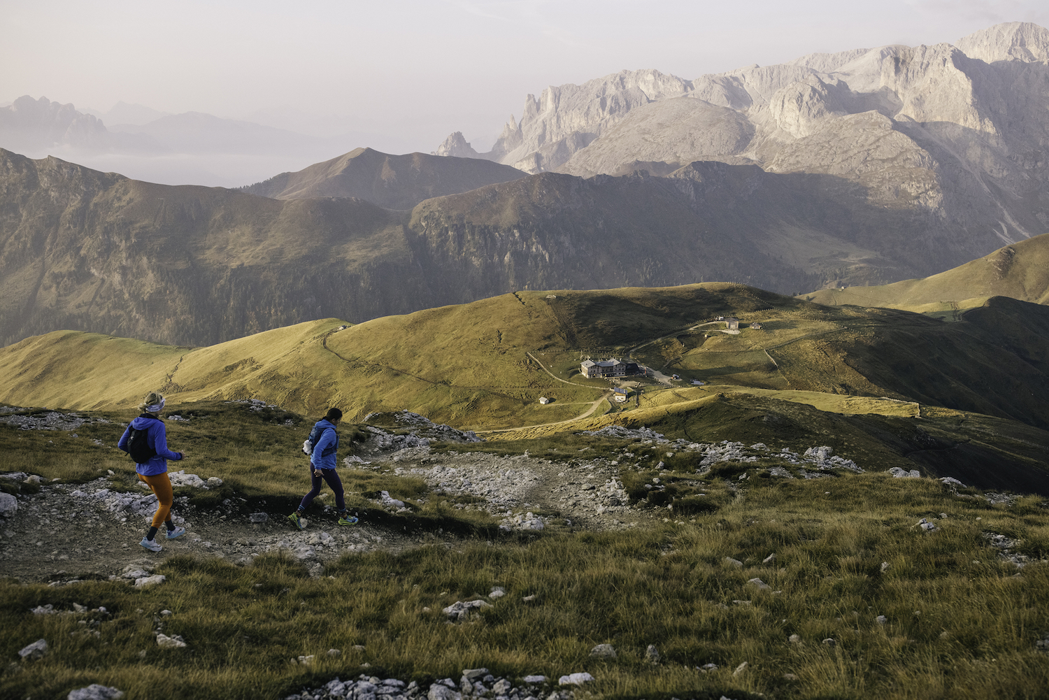 Two runners in descent towards a collection of mountain huts.