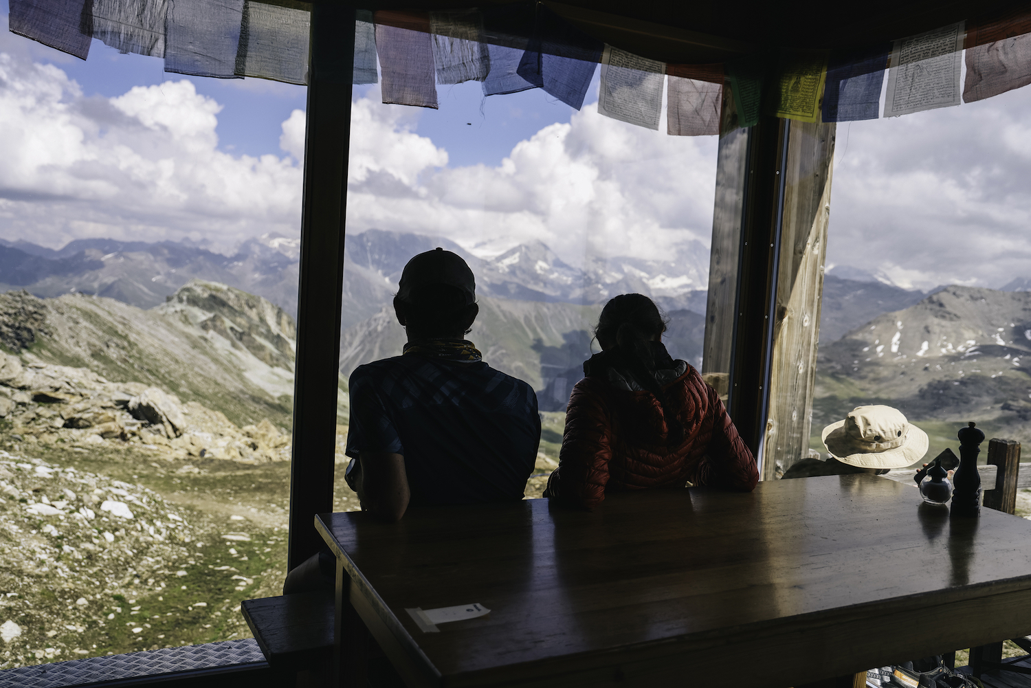 Two people sit on a bench looking at a mountain view.