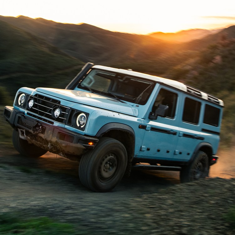 A 2026 Ineos Grenadier Station Wagon (or SUV) driving up a hill on a dirt track during a test drive