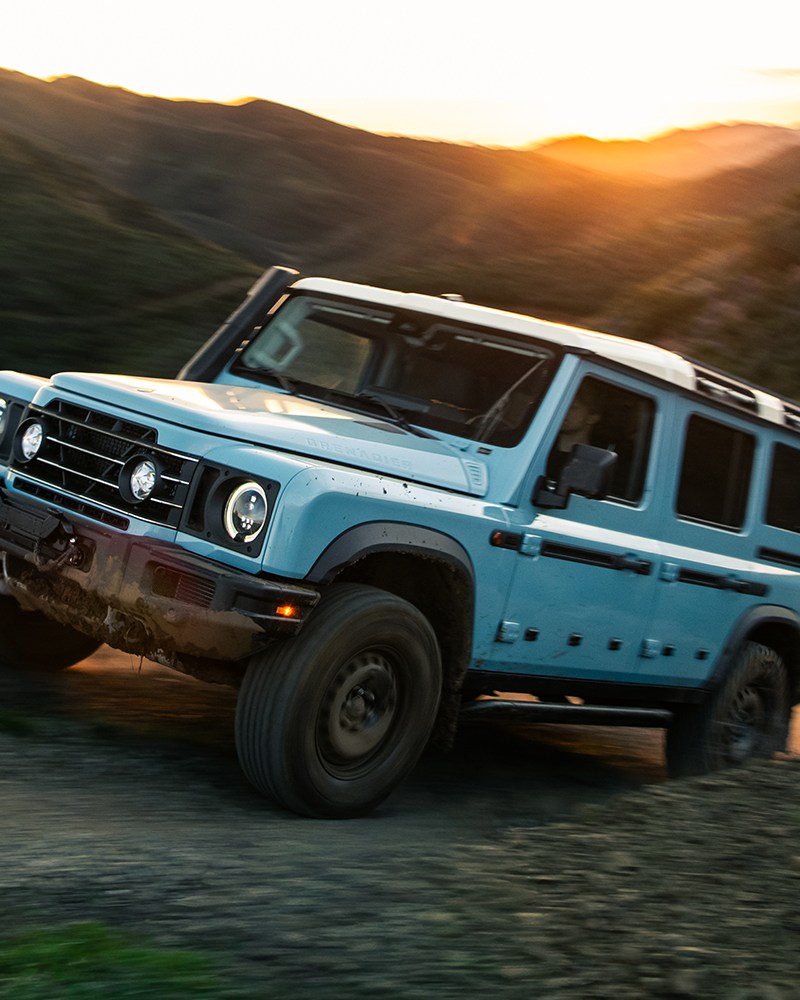 A 2026 Ineos Grenadier Station Wagon (or SUV) driving up a hill on a dirt track during a test drive