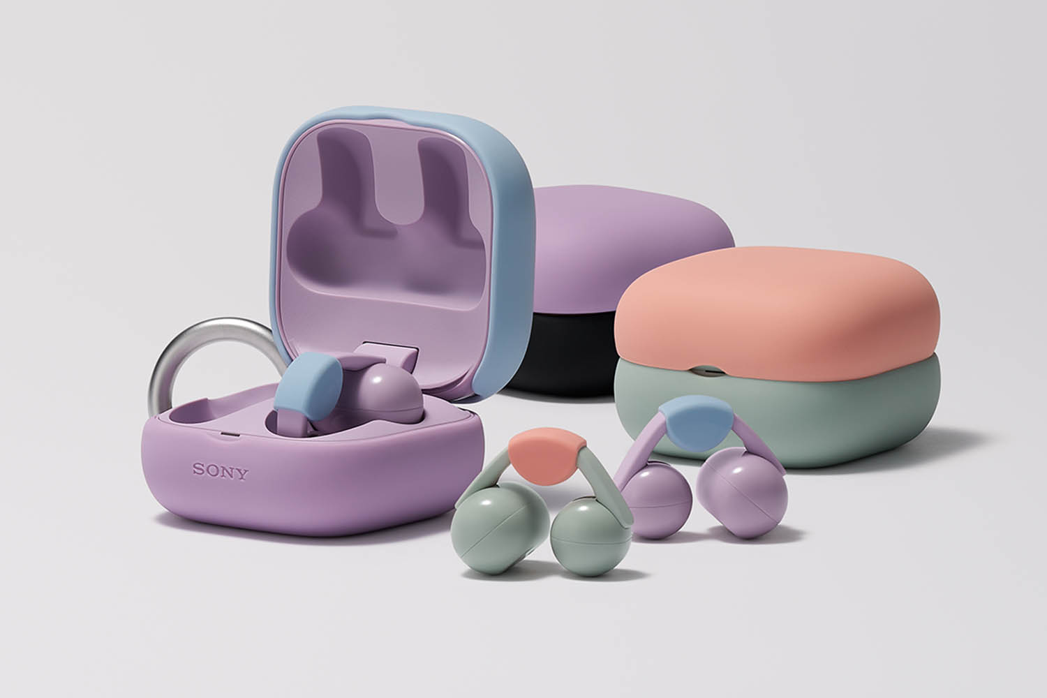 Wireless earbuds in purple and green sitting on a table next to three earbuds cases in purple, green, orange and black