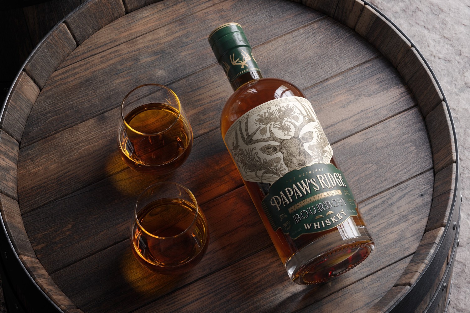 Bottle of bourbon and two glasses on top of a barrel