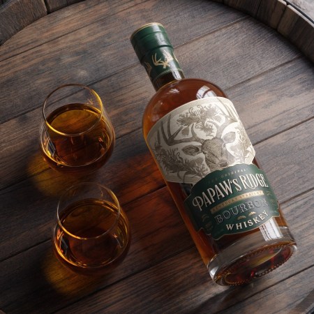 Bottle of bourbon and two glasses on top of a barrel