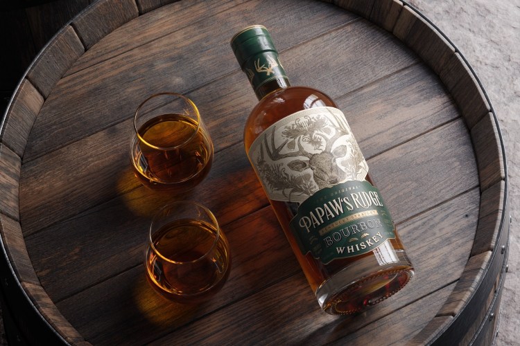 Bottle of bourbon and two glasses on top of a barrel