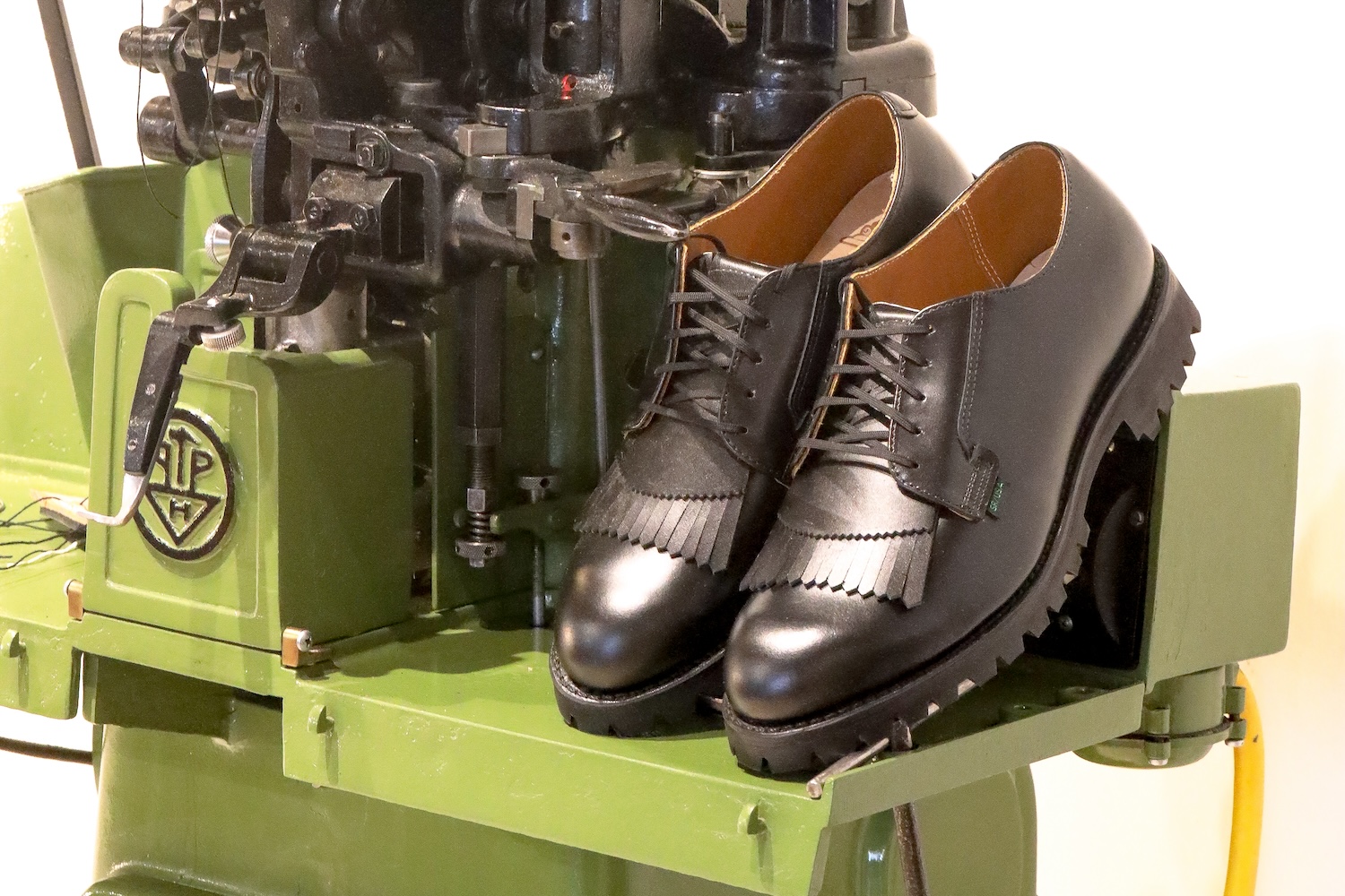 A pair of brown shoes sitting on a green shoemaking machine