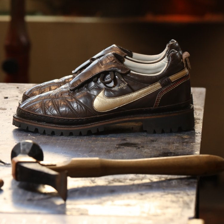 A pair of brown shoes on a table with a hammer in the foreground