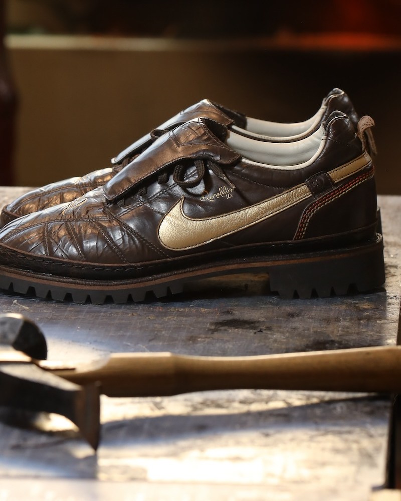 A pair of brown shoes on a table with a hammer in the foreground