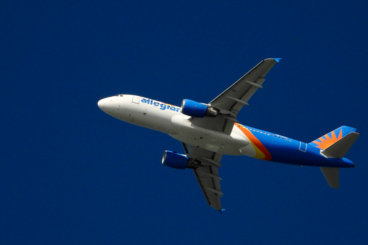 Allegiant Air commercial aircraft airborne, with its distinctive dark blue fuselage and gold sun logo visible.