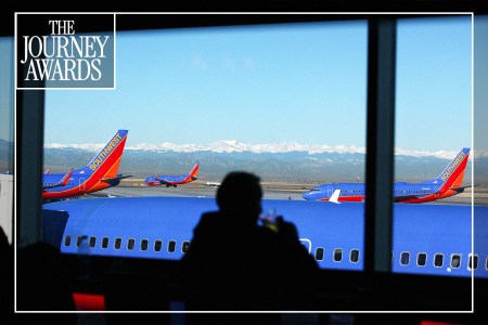 A passenger looking out at planes parked on the tarmac through an airport window.