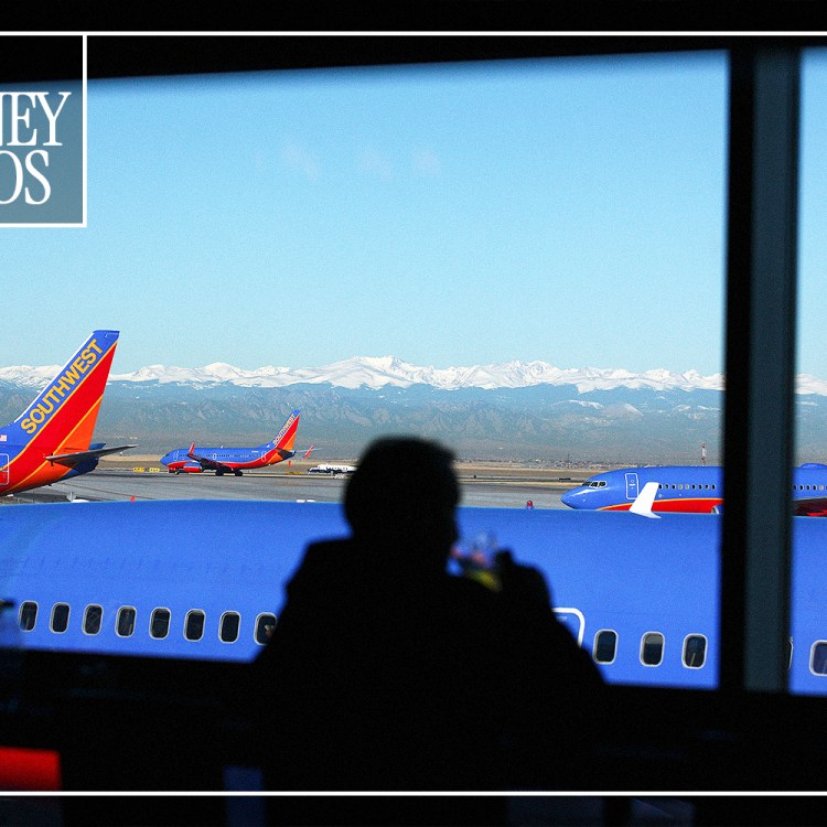 A passenger looking out at planes parked on the tarmac through an airport window.