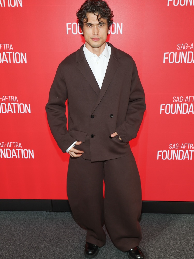 A man wearing big pants and a double breasted blazer in front of a red background