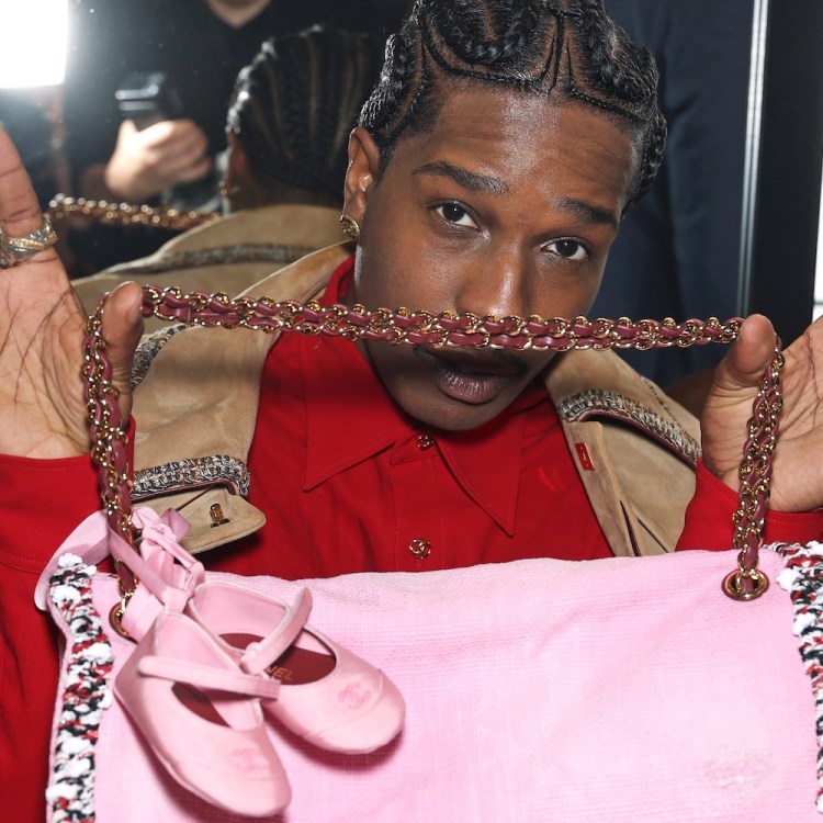 A man holding up a pink bag with baby ballet flats attached to the handle