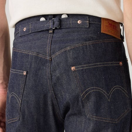 Close-up of the back of a person wearing dark wash denim jeans with a cinch-back, suspender buttons, and a Levi's patch.