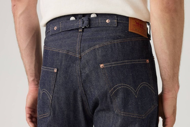Close-up of the back of a person wearing dark wash denim jeans with a cinch-back, suspender buttons, and a Levi's patch.