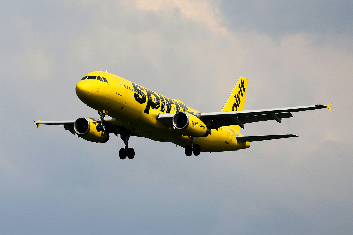 A bright yellow Spirit Airlines commercial aircraft flying through a clear blue sky.