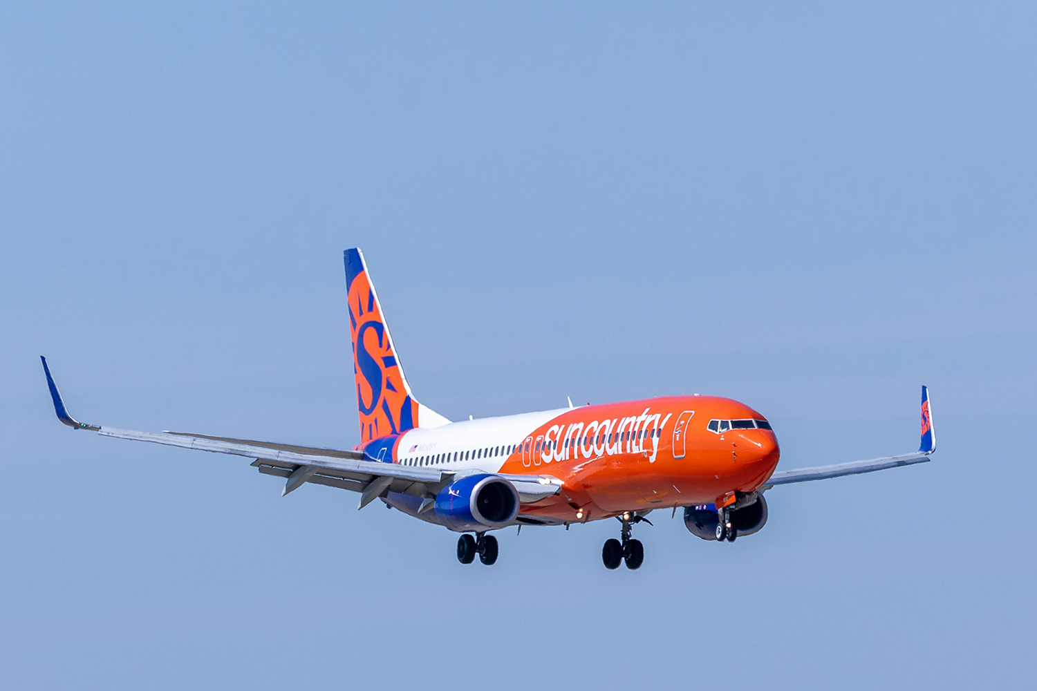 Sun Country Airlines plane in the sky, with its distinctive blue fuselage and yellow sun logo visible on the tail.