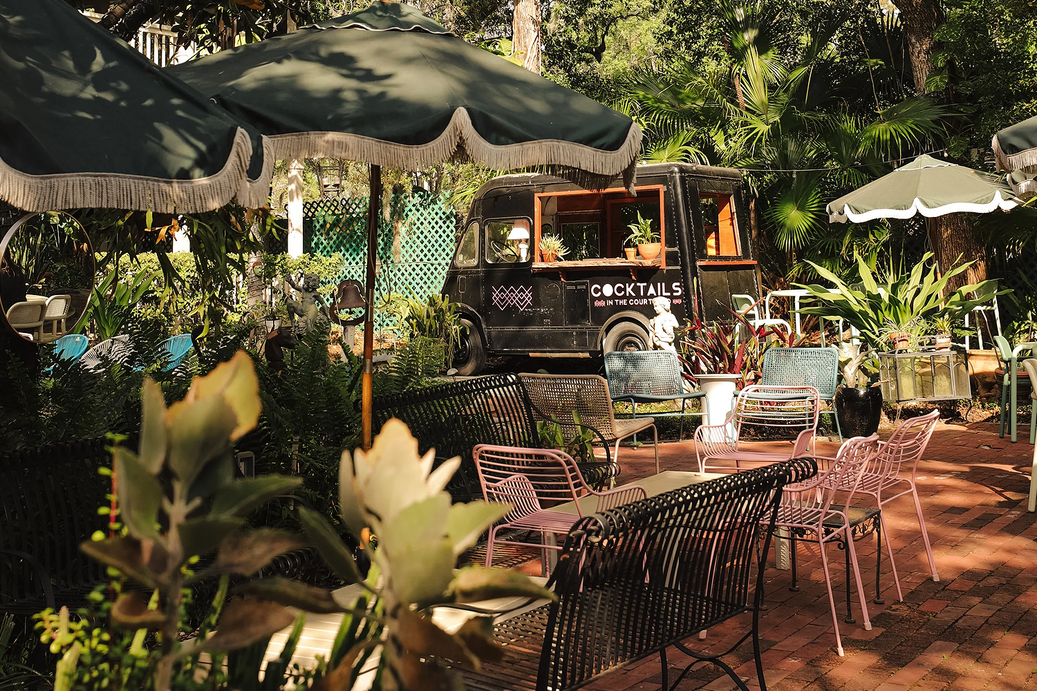 Outdoor courtyard at The Wellborn in Orlando featuring lush tropical greenery, string lights overhead, a mix of tables and lounge seating and a relaxed garden atmosphere centered around a historic building.