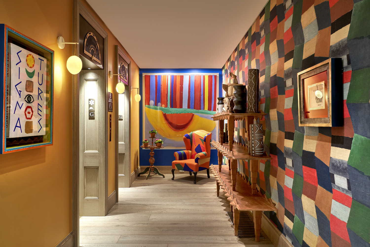 Interior hallway at Warren Street Hotel in New York featuring colorful patterned walls, framed artwork, textured carpeting and warm lighting.