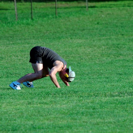 A man working out on all fours in a green field with a hat and headphones on