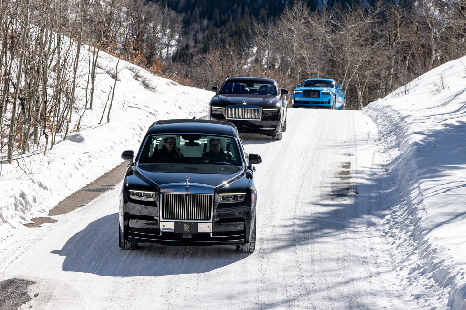 Three cars driving on a snowy road over the top of a hill