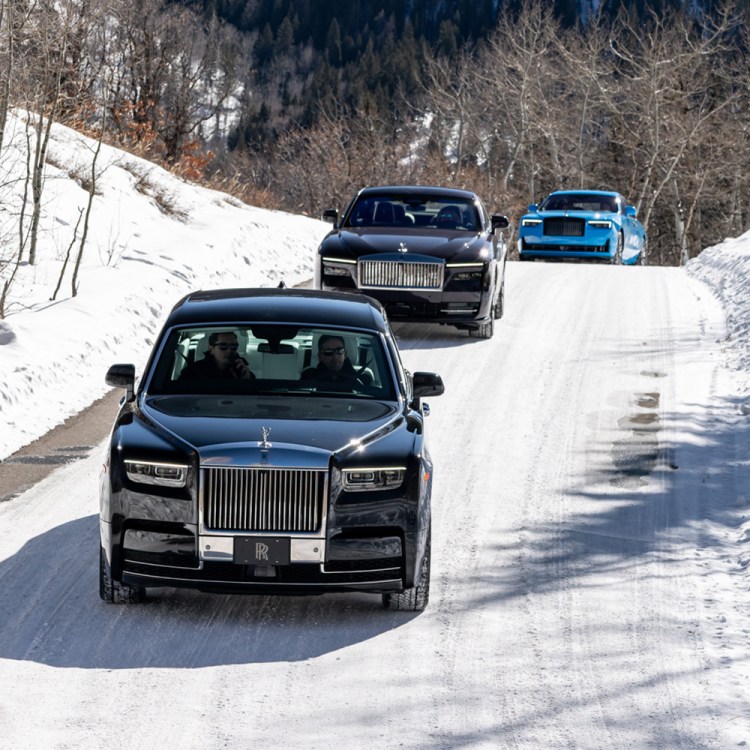 Three cars driving on a snowy road over the top of a hill
