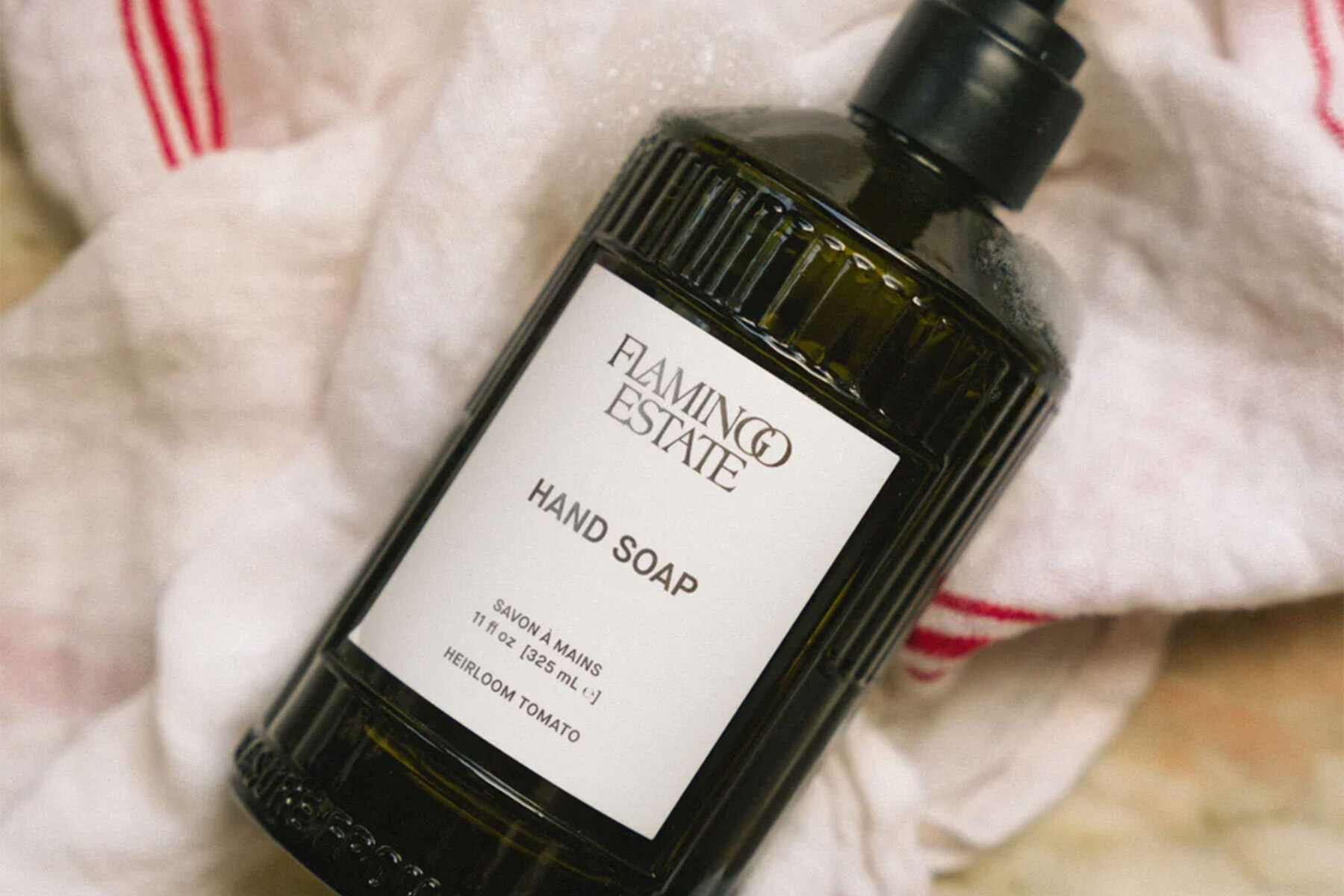 A green glass bottle with a white label lying on a white towel with red stripes