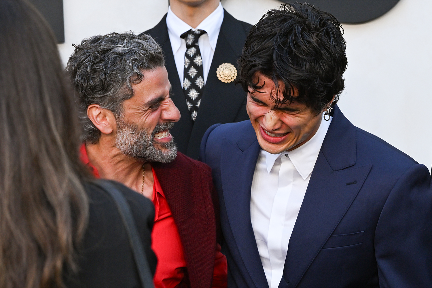 Two men laughing while dressed in suits with a third man in a tie behind them