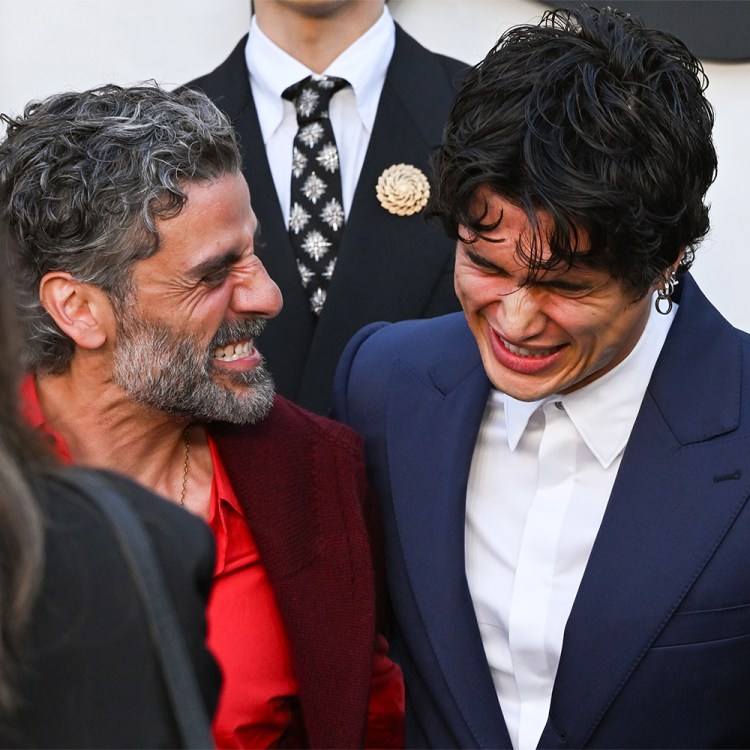 Two men laughing while dressed in suits with a third man in a tie behind them