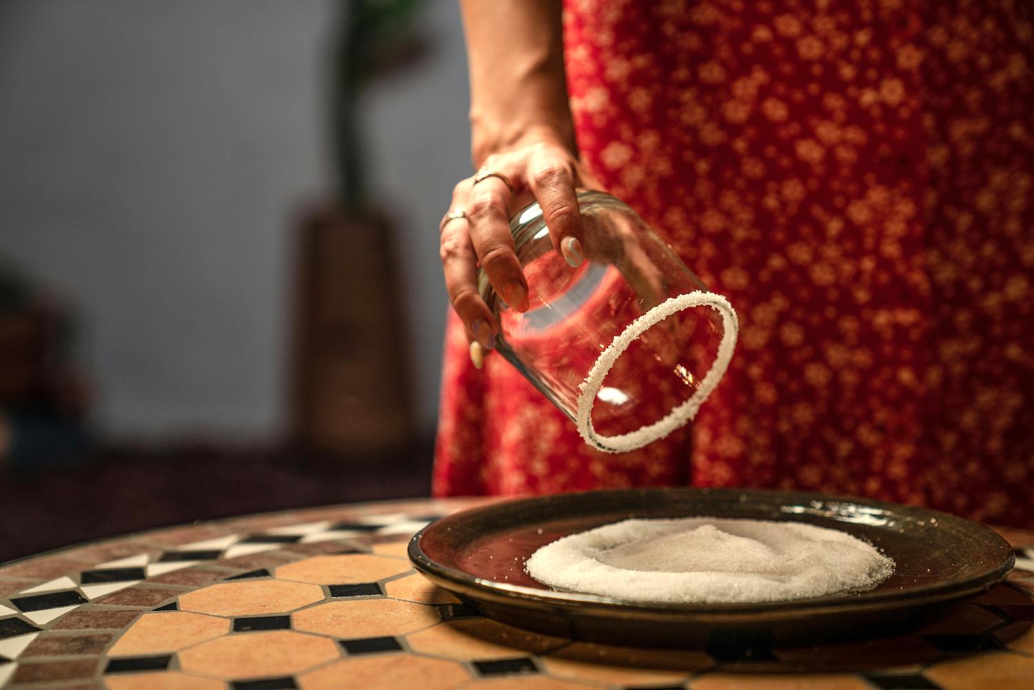 a woman in a red floral dress rimming a rocks glass with salt on a mosaic table