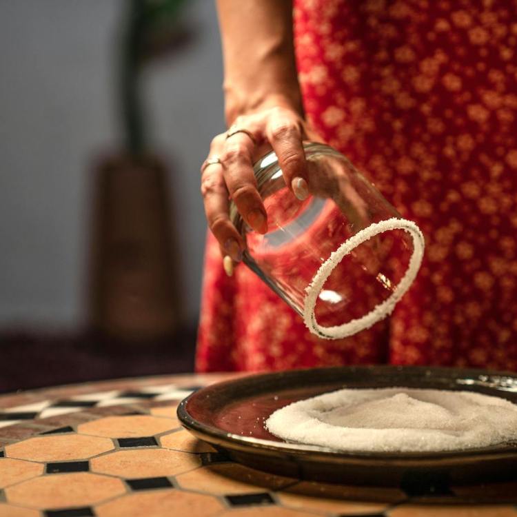 a woman in a red floral dress rimming a rocks glass with salt on a mosaic table