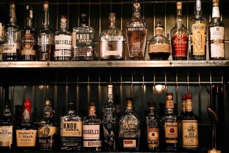 two rows of bourbon bottles sitting on a weathered metal backbar