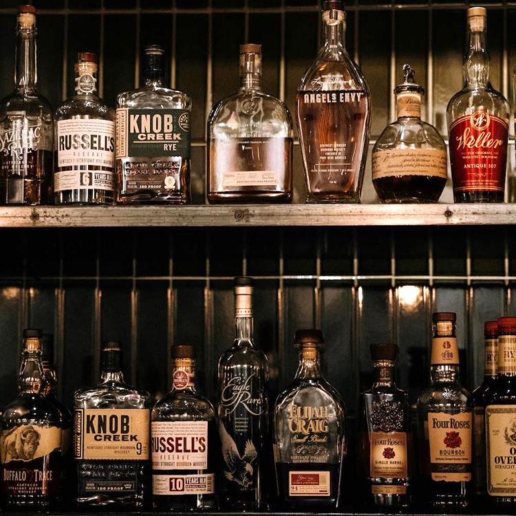 two rows of bourbon bottles sitting on a weathered metal backbar