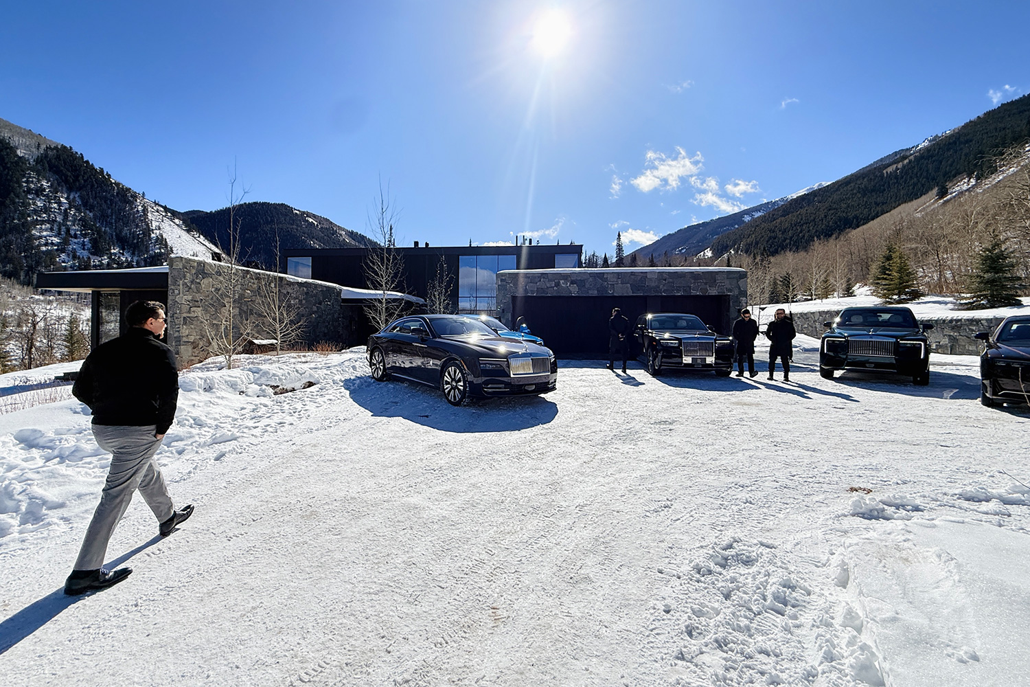 A man walking up to a mountainside house with four cars parked in front