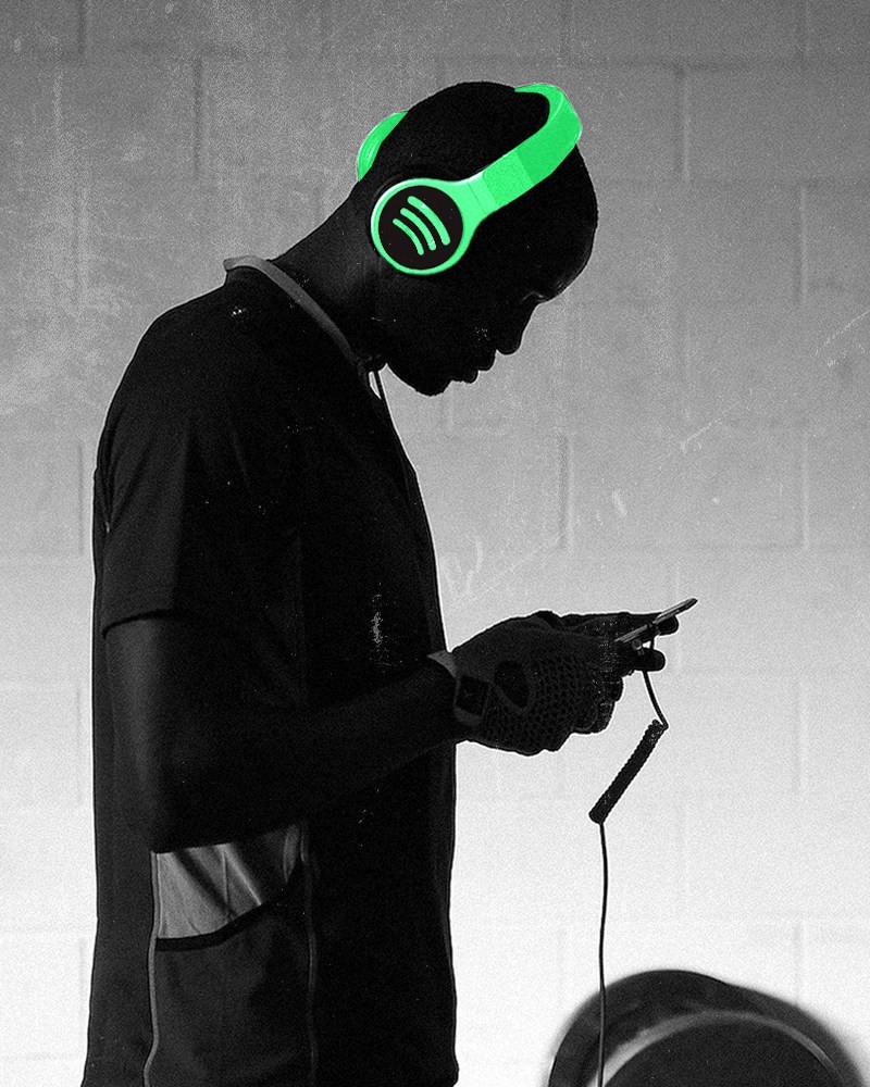 A man looking at a phone, wearing headphones with a lime-green Spotify illustration.