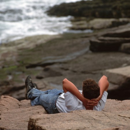 A man laying against the rocks, doing nothing.