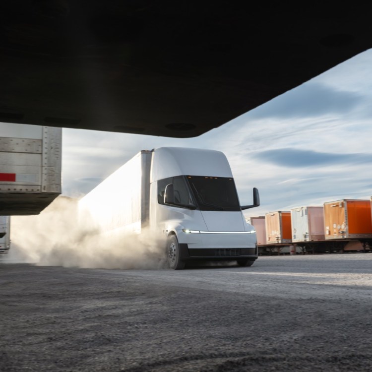 A white semi driving with cargo in the background