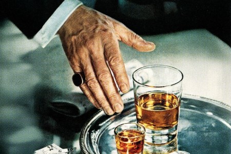 A man reaching for a glass of whiskey