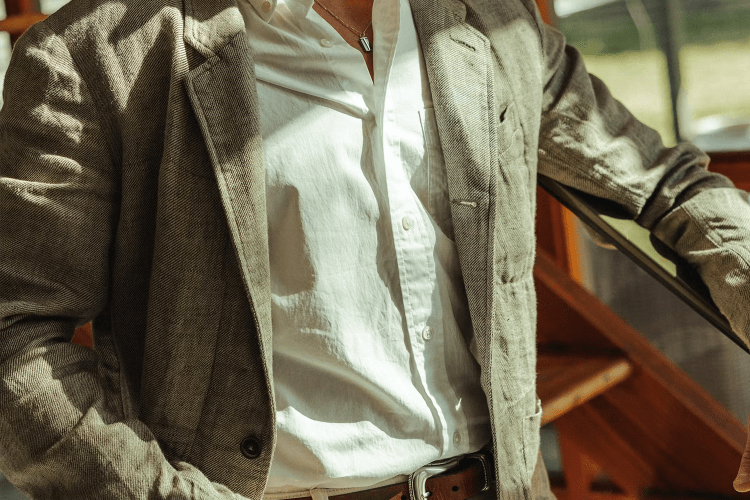 lifestyle image of man wearing white button down with a neutral colored blazer over it in sunlight