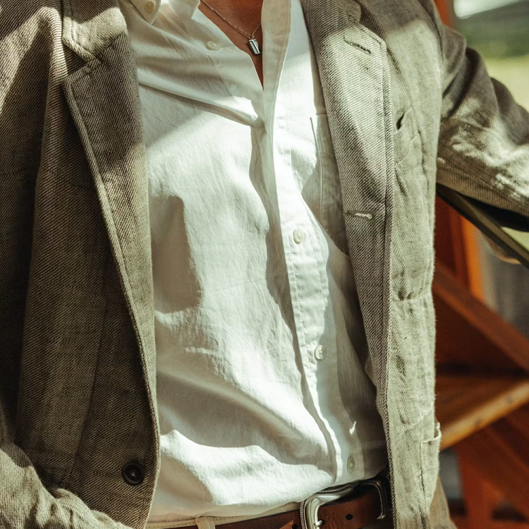 lifestyle image of man wearing white button down with a neutral colored blazer over it in sunlight