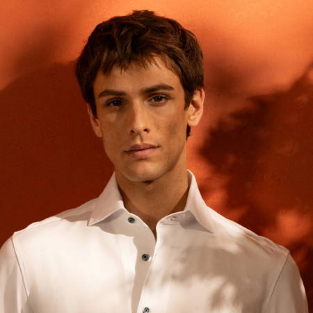A man in a white shirt standing against an orange wall