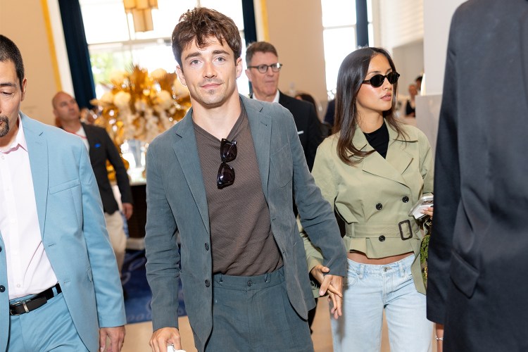 A man in a blazer with a T-shirt and sunglasses hanging from the neck holding the hand of a woman in sunglasses