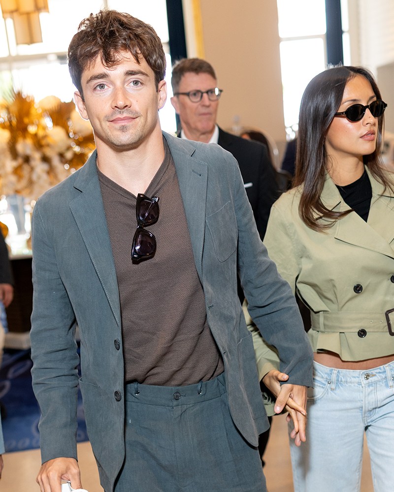 A man in a blazer with a T-shirt and sunglasses hanging from the neck holding the hand of a woman in sunglasses