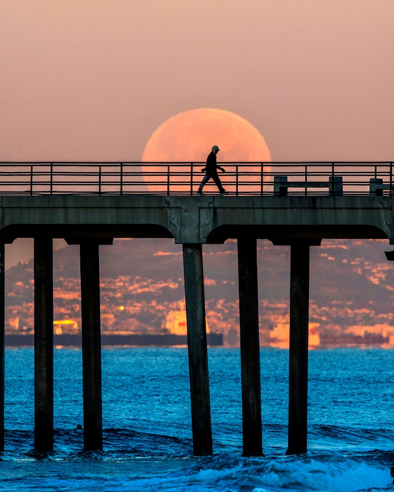 A man walking on a boardwalk in front of a super moon.