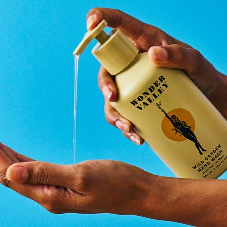 A hand pressing the top of a hand soap bottle with the soap falling onto an open palm with a blue background