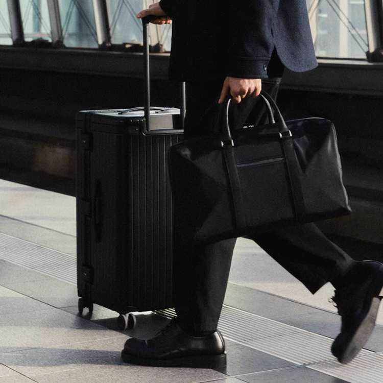 Carl Friedrik lifestyle image of man holding weekender bag pushing suitcase