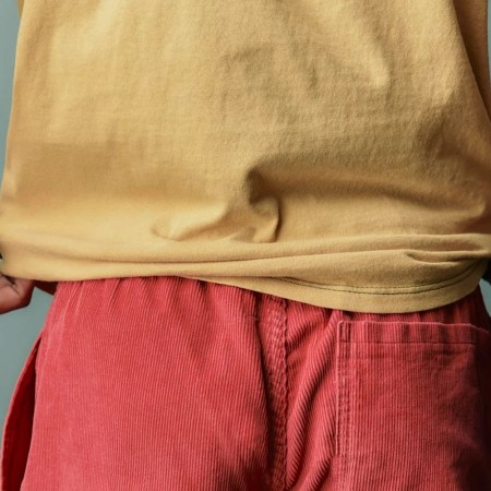 A model wearing a yellow shirt and red cord shorts.
